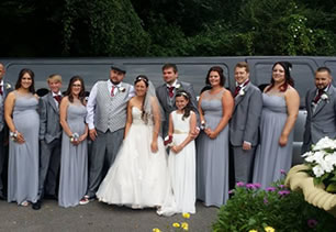Bride, groom, bridesmaids and guests stand with wedding limousine